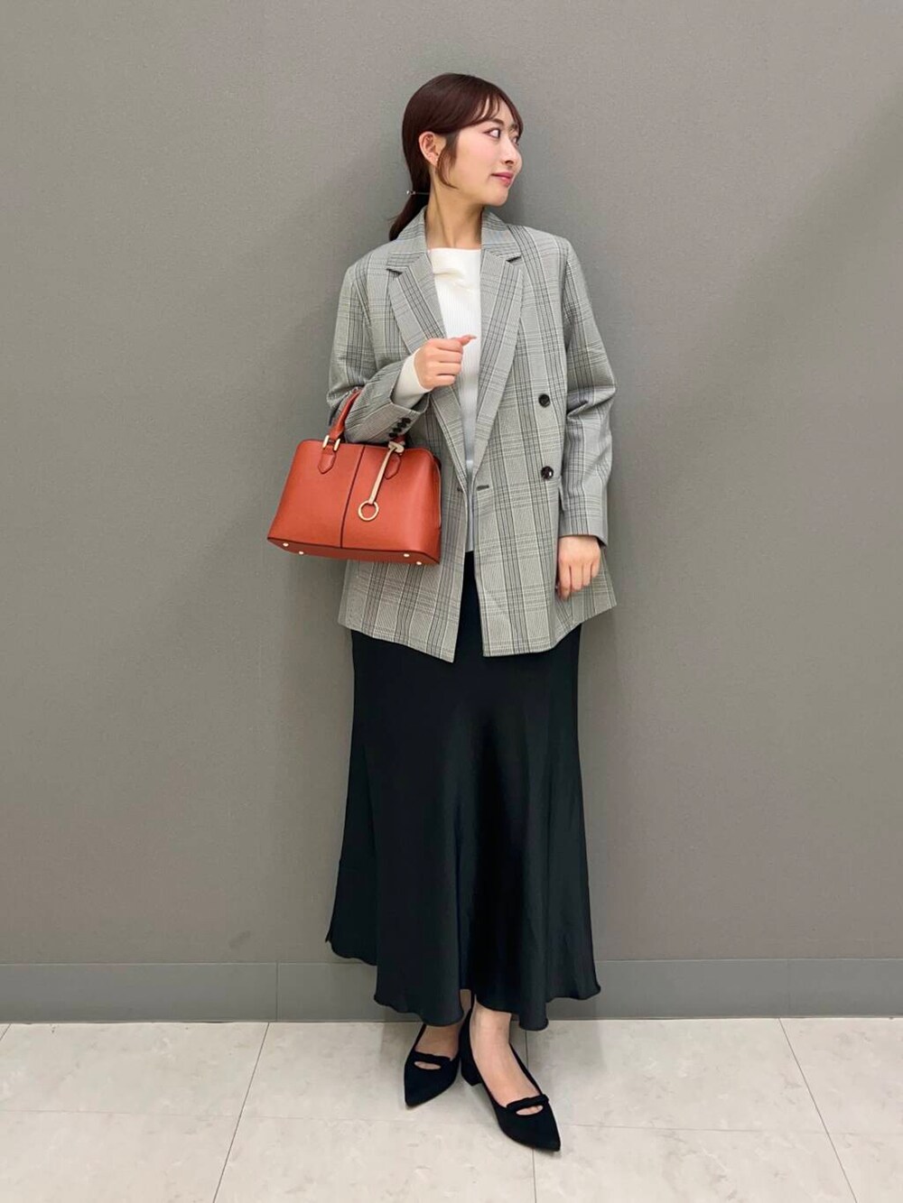 オレンジ系のハンドバッグ、ブラック系のパンプス、ブラック系のスカートを着用したレディースの春コーディネートの2枚目の写真