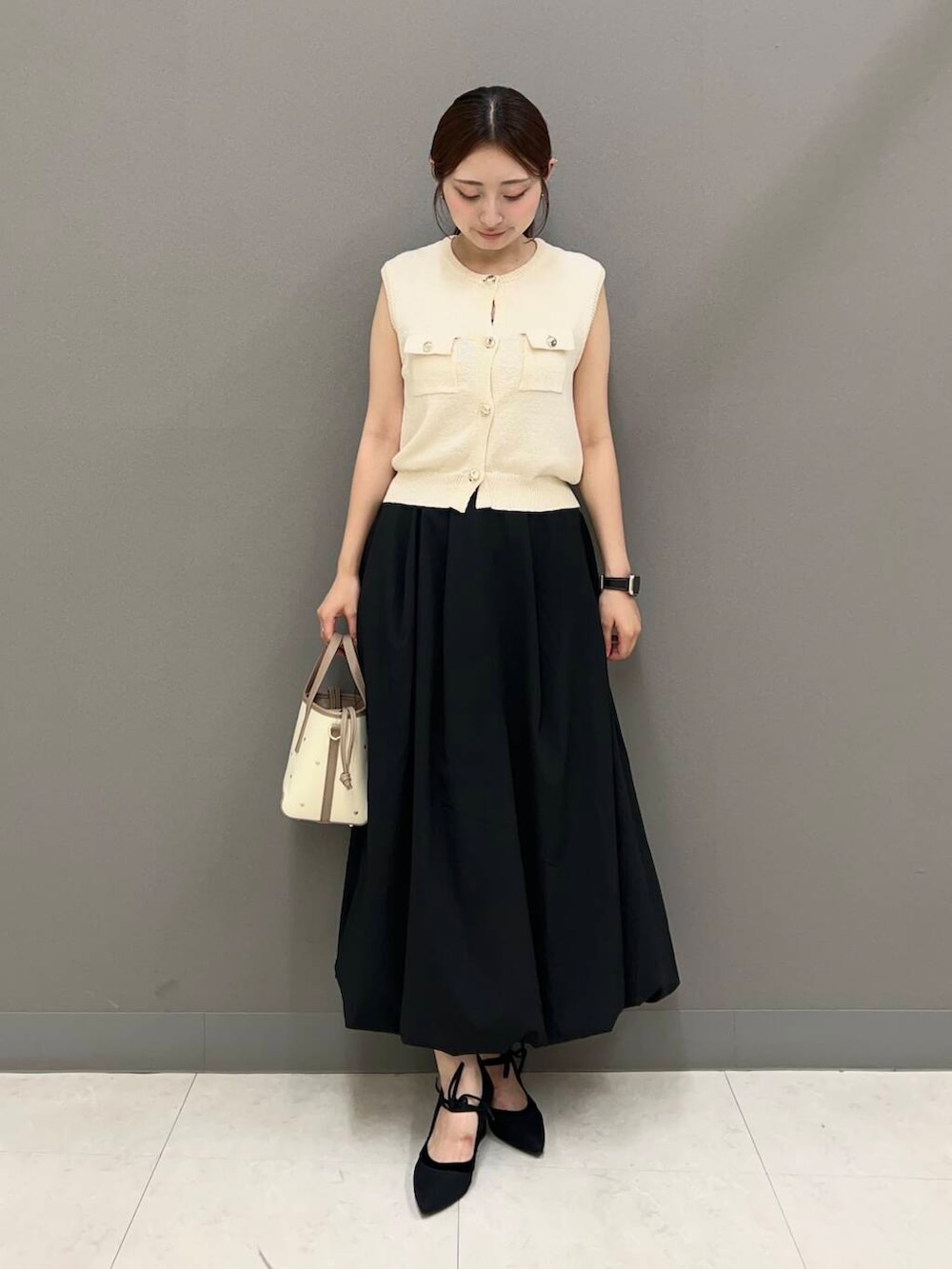 ブラック系のパンプス、ブラック系のスカート、ホワイト系のベストを着用したレディースの夏コーディネートの2枚目の写真