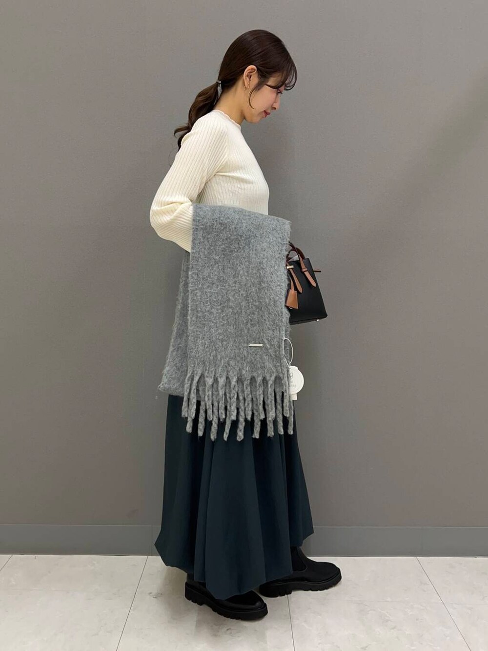 ブラック系のハンドバッグ、ブルー系のスカート、ブラック系のブーツを着用したレディースの冬コーディネートの2枚目の写真