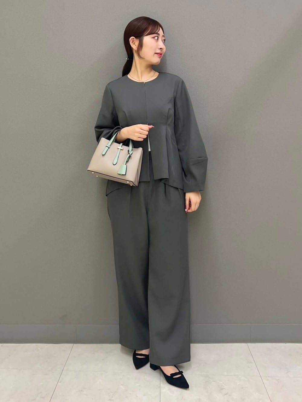 グリーン系のハンドバッグ、ブラック系のパンプス、グレー系のワンピースを着用したレディースの春コーディネートの2枚目の写真