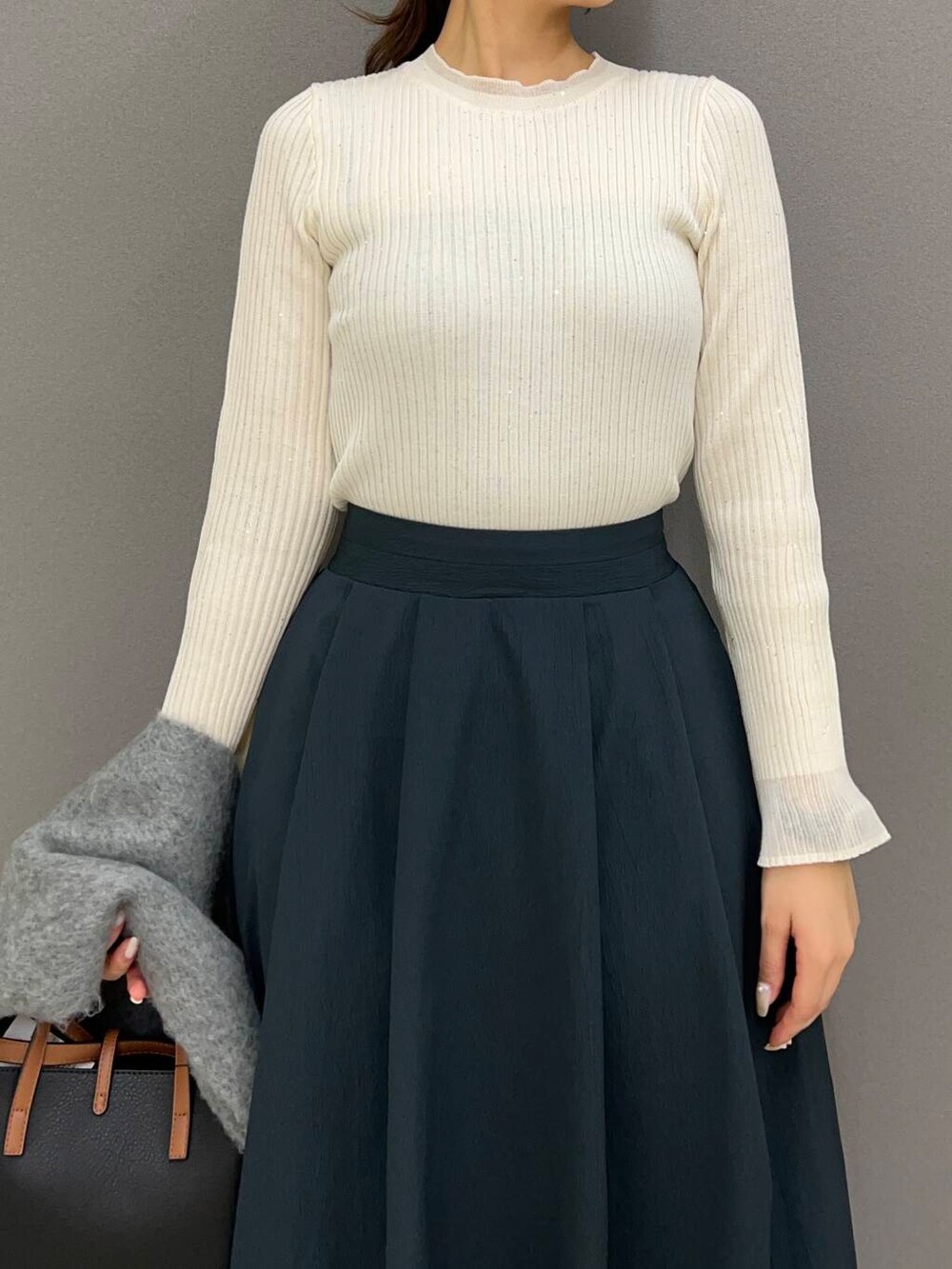 ブラック系のハンドバッグ、ブルー系のスカート、ブラック系のブーツを着用したレディースの冬コーディネートの3枚目の写真