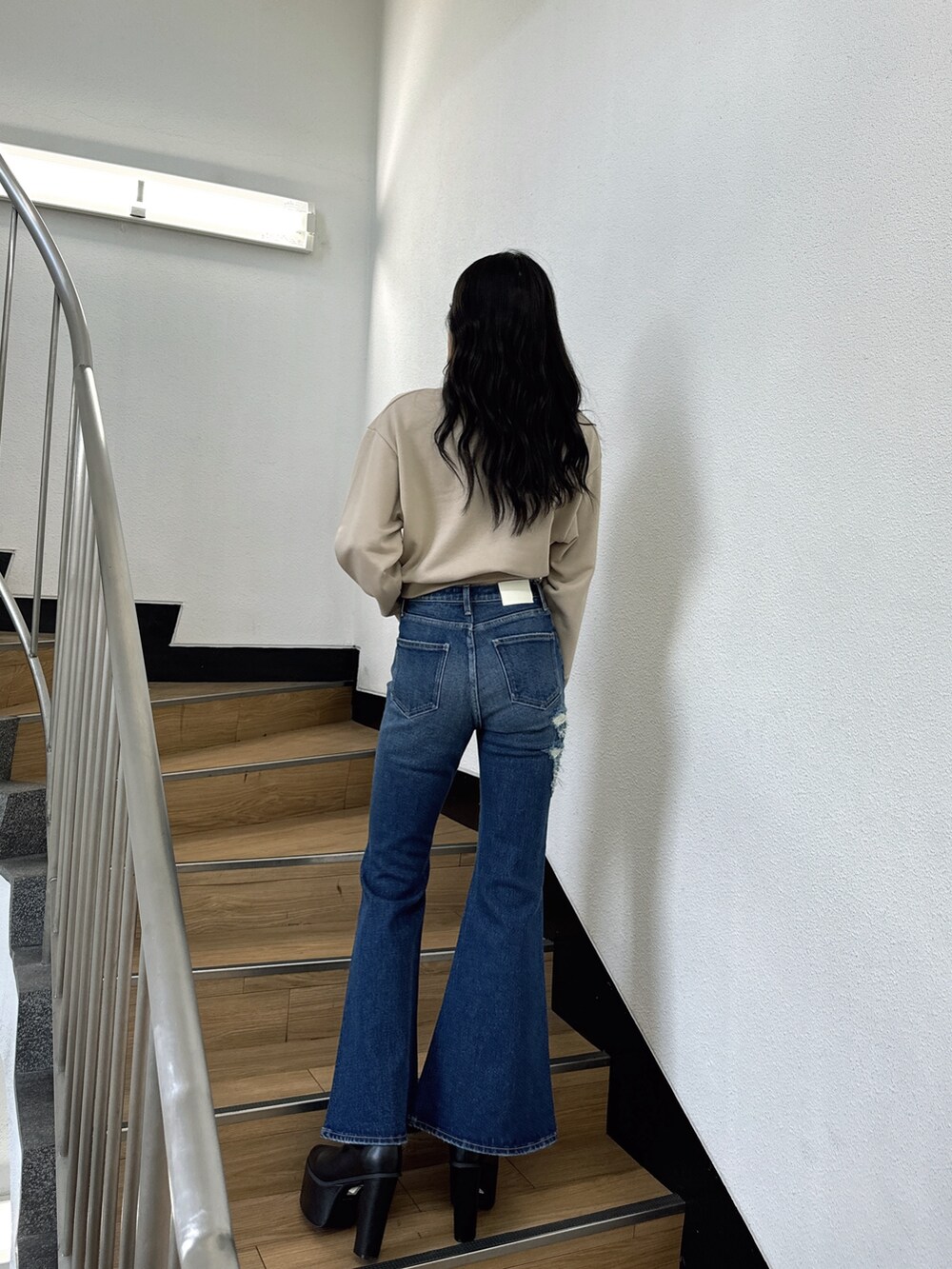 ベージュ系のスウェット、ブルー系のデニムパンツ、ブラック系のブーツを着用したレディースの夏コーディネートの2枚目の写真