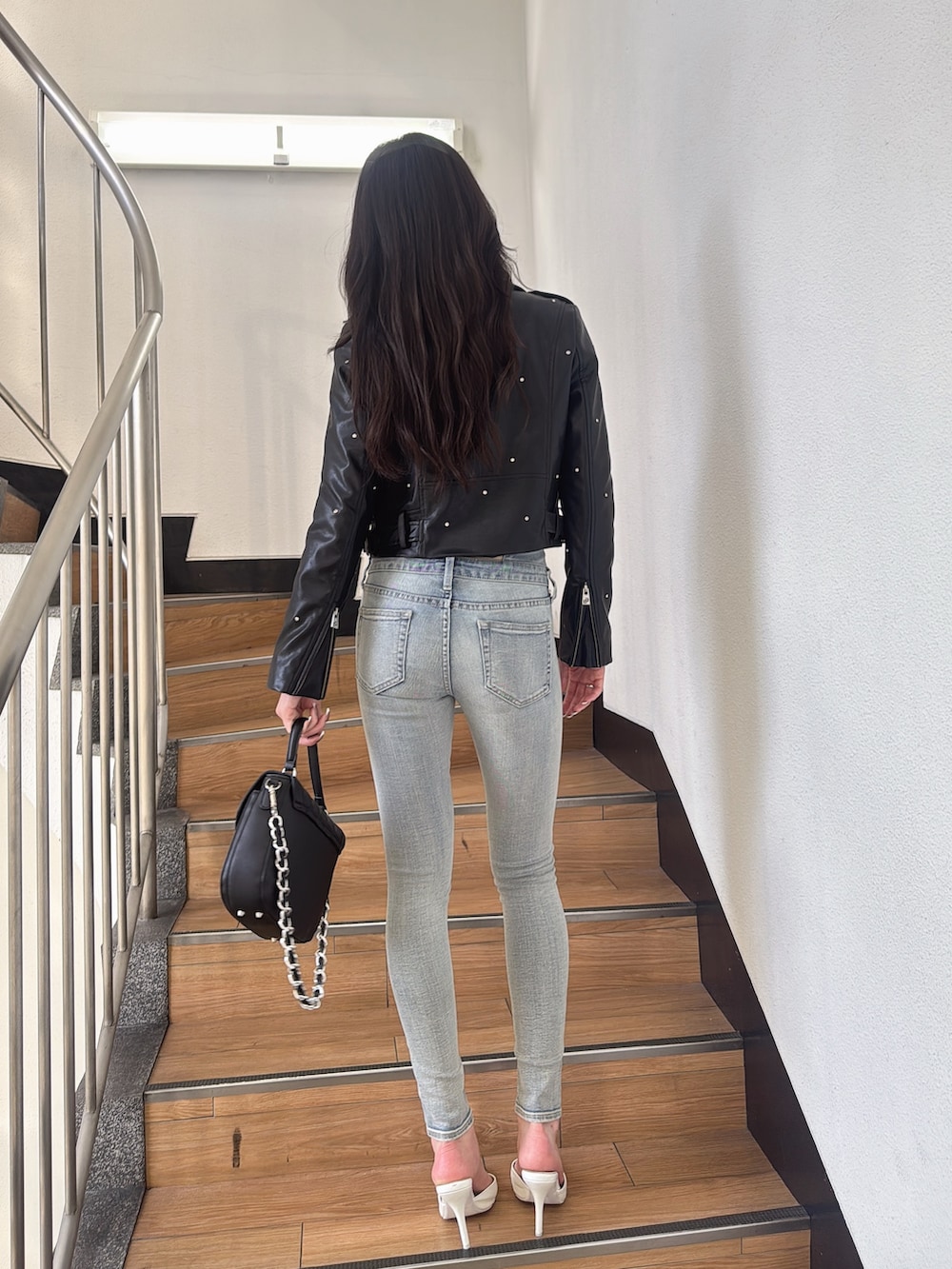 ブラック系のライダースジャケット、ブルー系のデニムパンツ、ブラック系のハンドバッグを着用したレディースの秋コーディネートの3枚目の写真