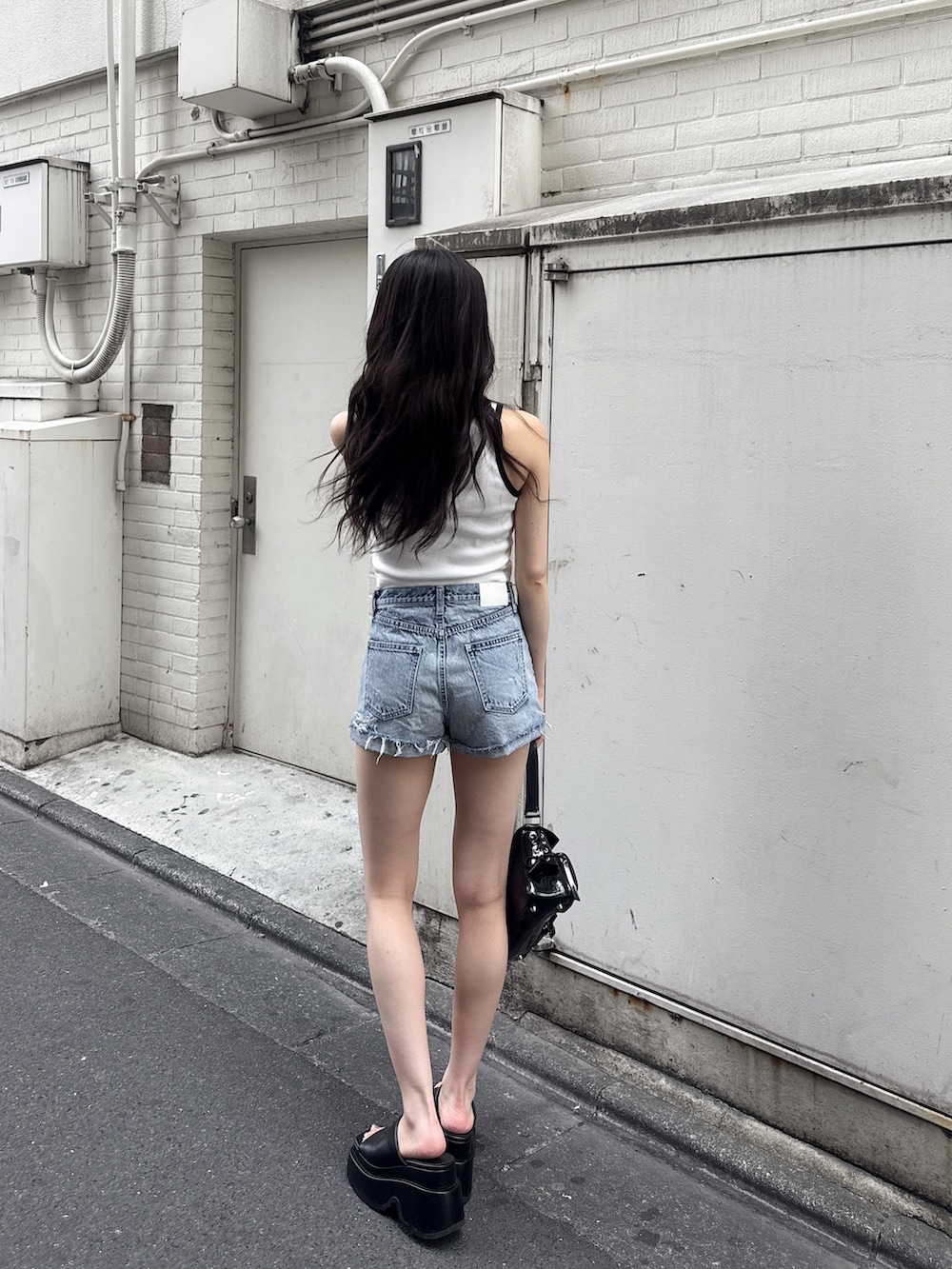 ホワイト系のタンクトップ、ブルー系のデニムパンツ、ブラック系のハンドバッグを着用したレディースの夏コーディネートの3枚目の写真