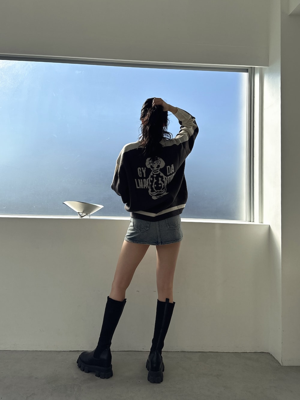 グレー系のニット/セーター、ブルー系のデニムスカート、ブラック系のブーツを着用したレディースの冬コーディネートの2枚目の写真