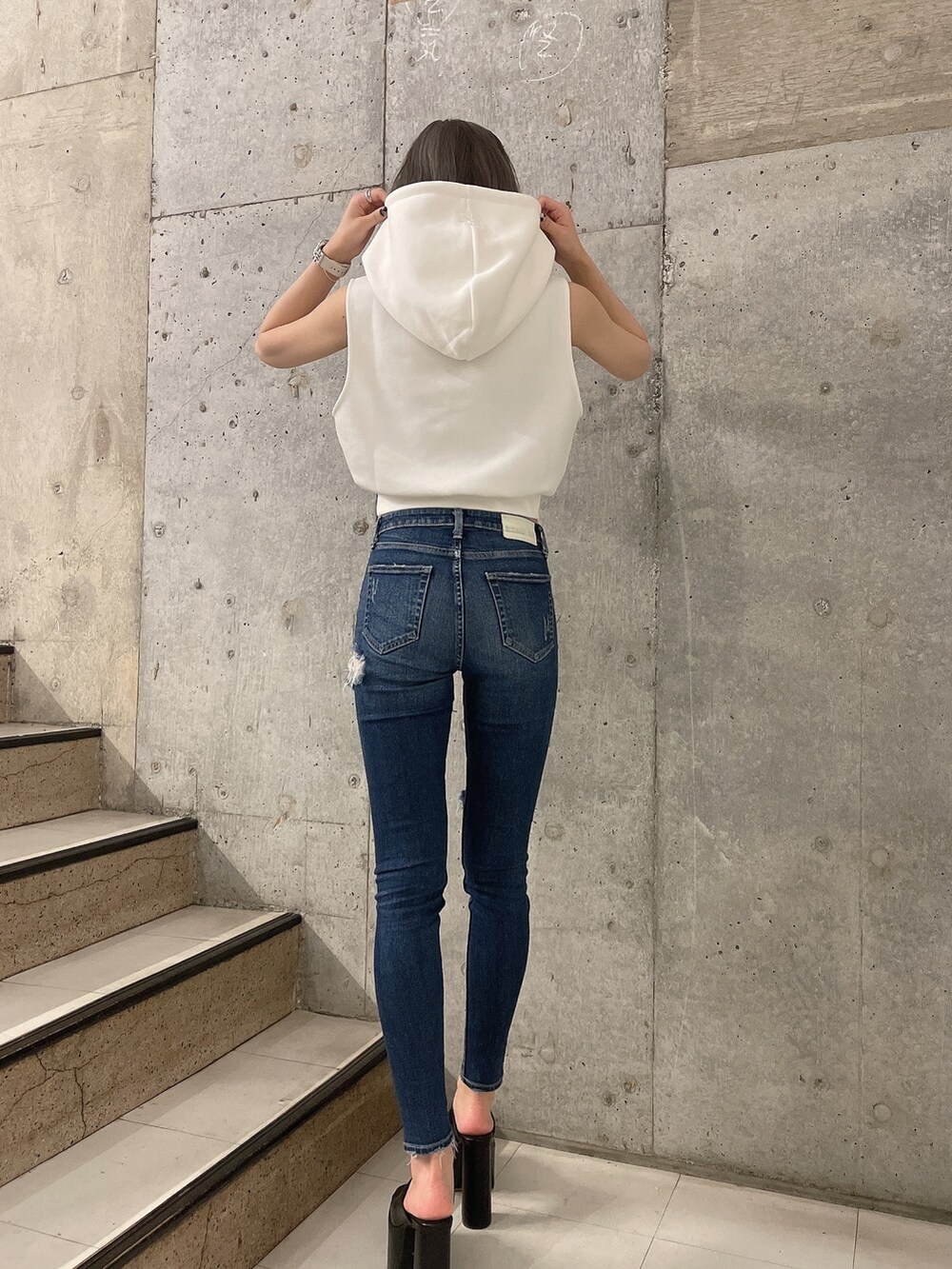 ホワイト系のパーカー、ブラック系のサンダル、ブルー系のデニムパンツを着用したレディースの夏コーディネートの2枚目の写真