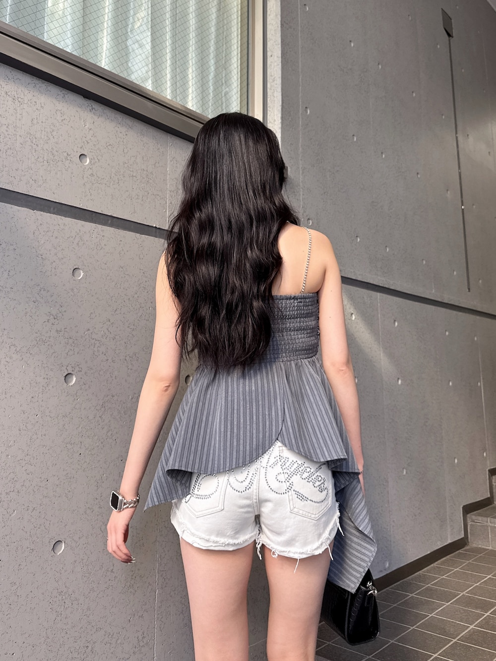 グレー系のキャミソール、ブラック系のサンダル、ホワイト系のデニムパンツを着用したレディースの春コーディネートの2枚目の写真