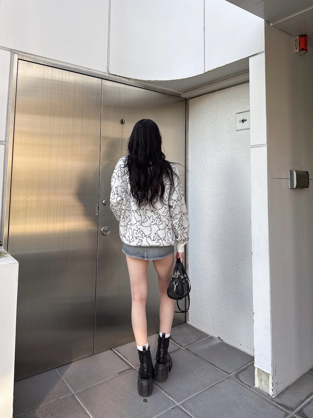 ホワイト系のニット/セーター、ブルー系のデニムスカート、ブラック系のブーツを着用したレディースの冬コーディネートの2枚目の写真