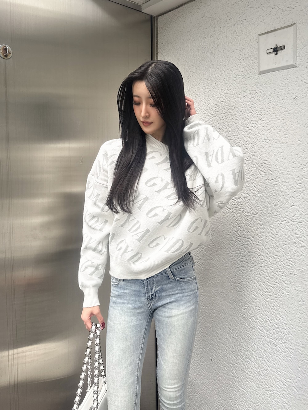 ホワイト系のニット/セーター、ホワイト系のショルダーバッグ、ブルー系のデニムパンツを着用したレディースの秋コーディネートの2枚目の写真