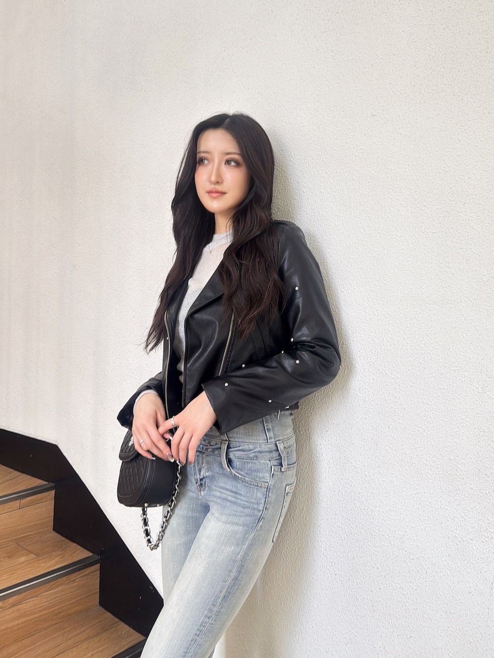 ブラック系のライダースジャケット、ブルー系のデニムパンツ、ブラック系のハンドバッグを着用したレディースの秋コーディネートの2枚目の写真