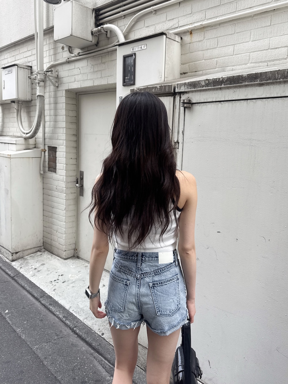 ホワイト系のタンクトップ、ブルー系のデニムパンツ、ブラック系のハンドバッグを着用したレディースの夏コーディネートの4枚目の写真