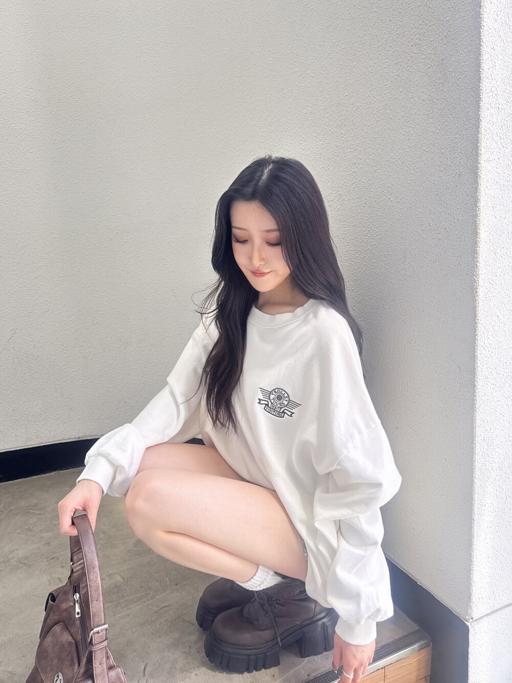 ホワイト系のスウェット、ブルー系のデニムスカート、ブラウン系のブーツを着用したレディースの夏コーディネートの4枚目の写真