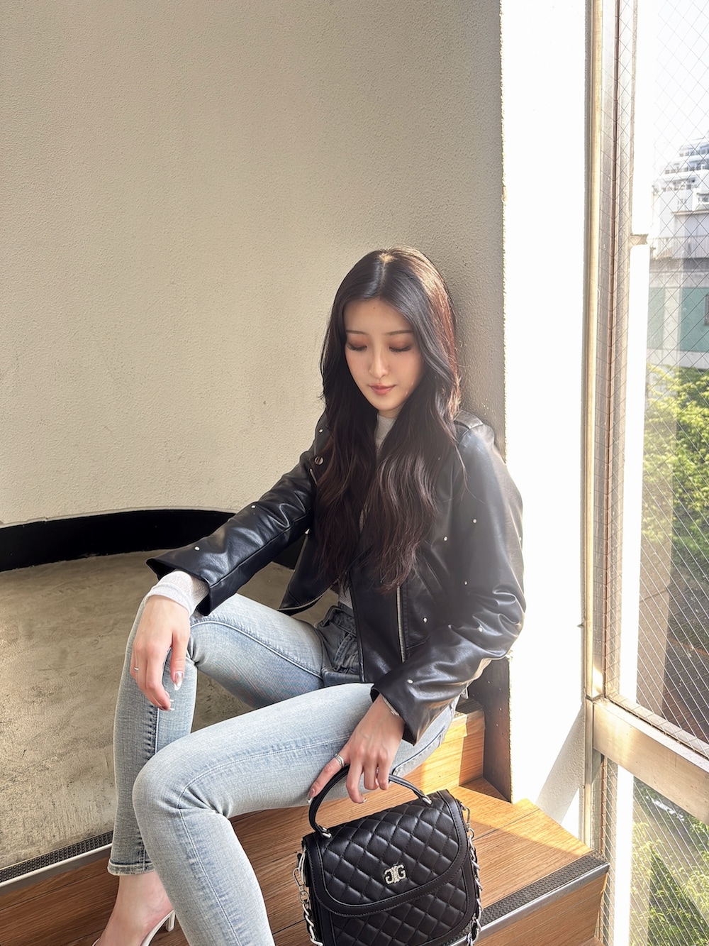 ブラック系のライダースジャケット、ブルー系のデニムパンツ、ブラック系のハンドバッグを着用したレディースの秋コーディネートの4枚目の写真