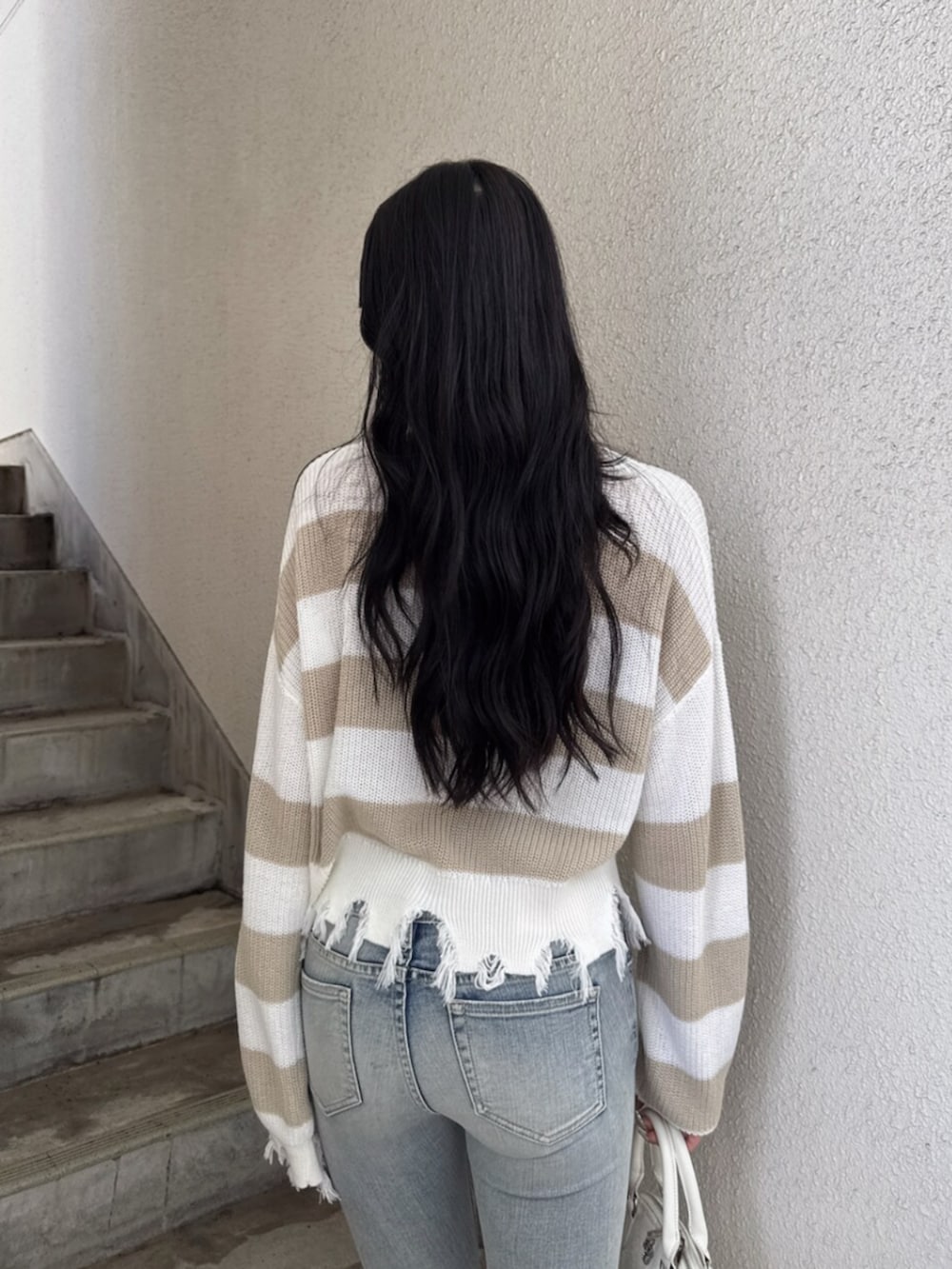 ベージュ系のニット/セーター、ブルー系のデニムパンツ、ホワイト系のハンドバッグを着用したレディースの夏コーディネートの5枚目の写真