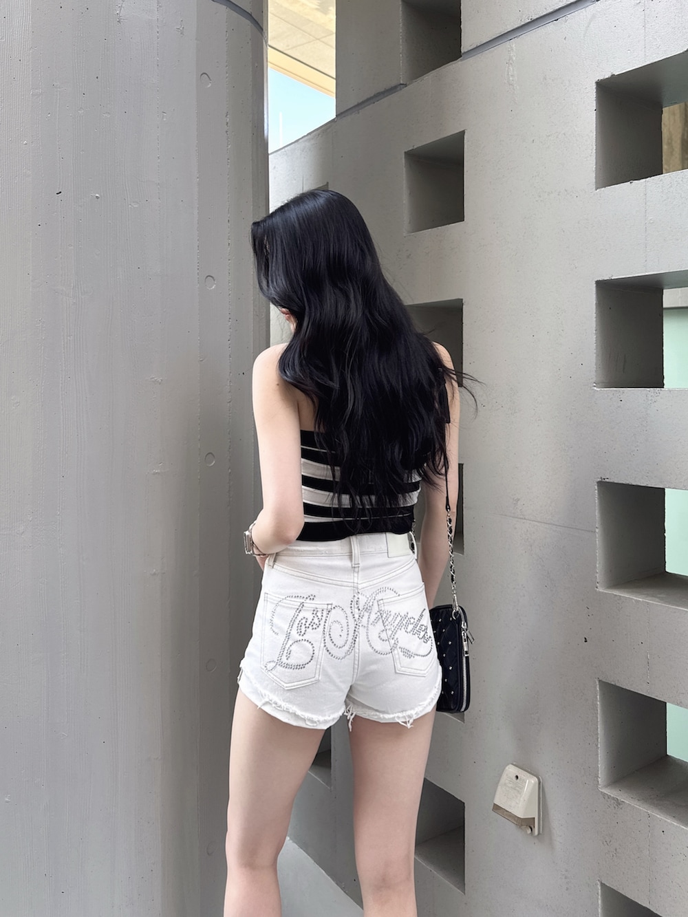 ブラック系のニット/セーター、ホワイト系のデニムパンツ、ブラック系のサンダルを着用したレディースの夏コーディネートの2枚目の写真