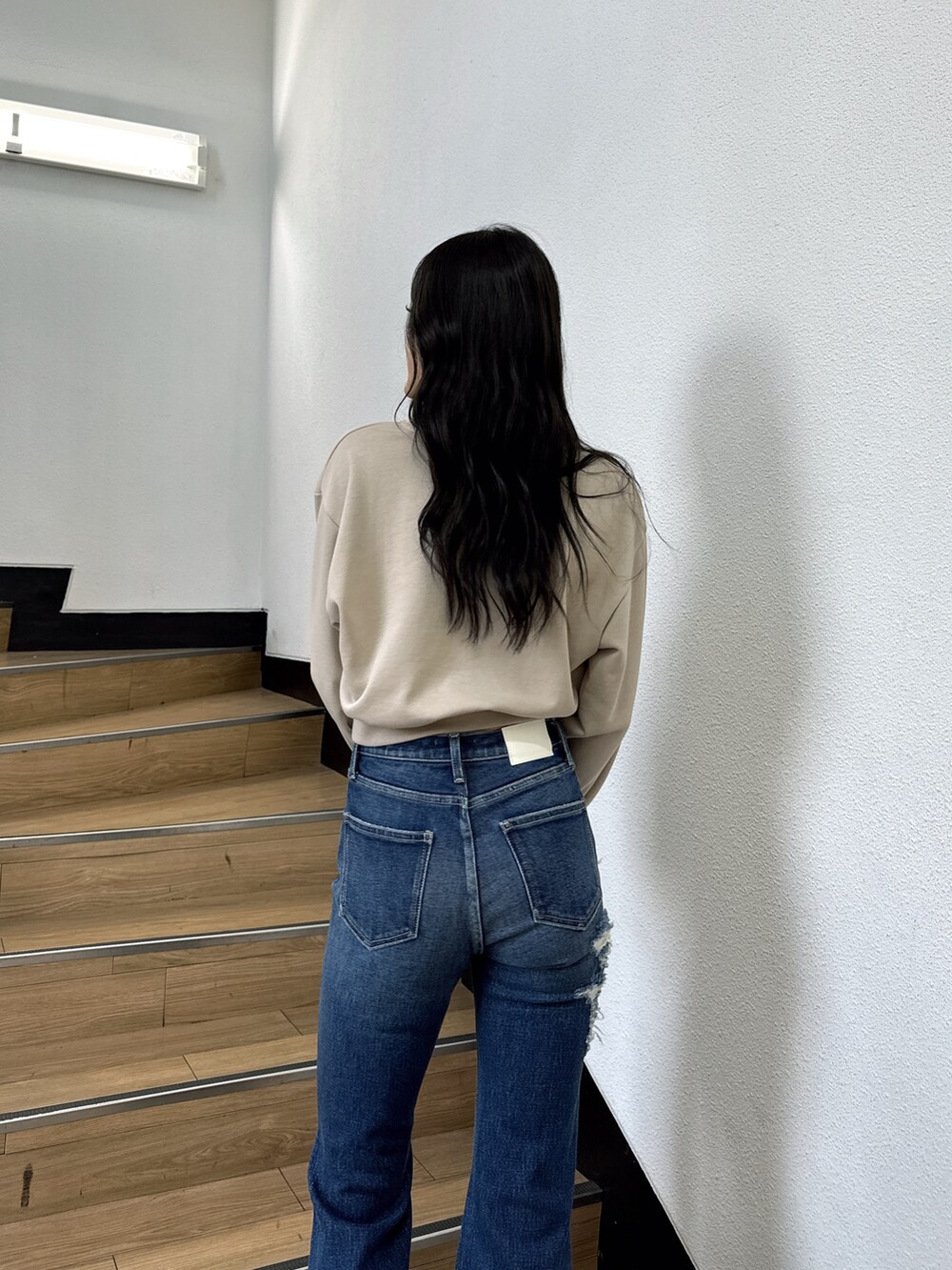 ベージュ系のスウェット、ブルー系のデニムパンツ、ブラック系のブーツを着用したレディースの夏コーディネートの4枚目の写真