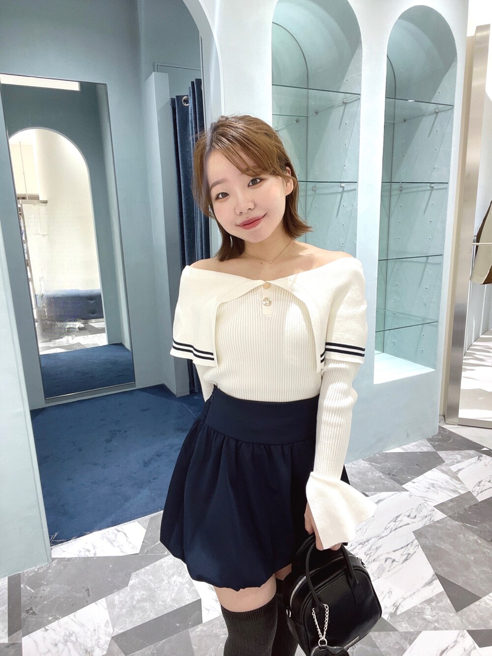 ホワイト系のニット/セーター、ブルー系のスカート、ブラック系のボストンバッグを着用したレディースの春コーディネートの3枚目の写真
