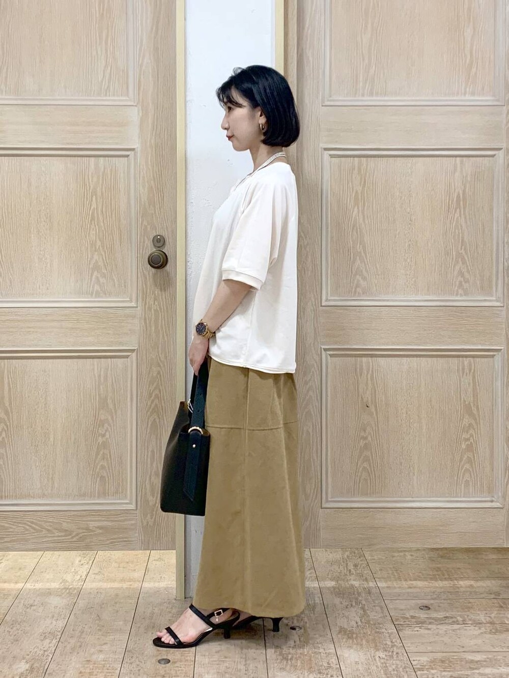 ブラック系のショルダーバッグ、ブラック系のサンダル、ベージュ系のTシャツ/カットソーを着用したレディースの秋コーディネートの2枚目の写真