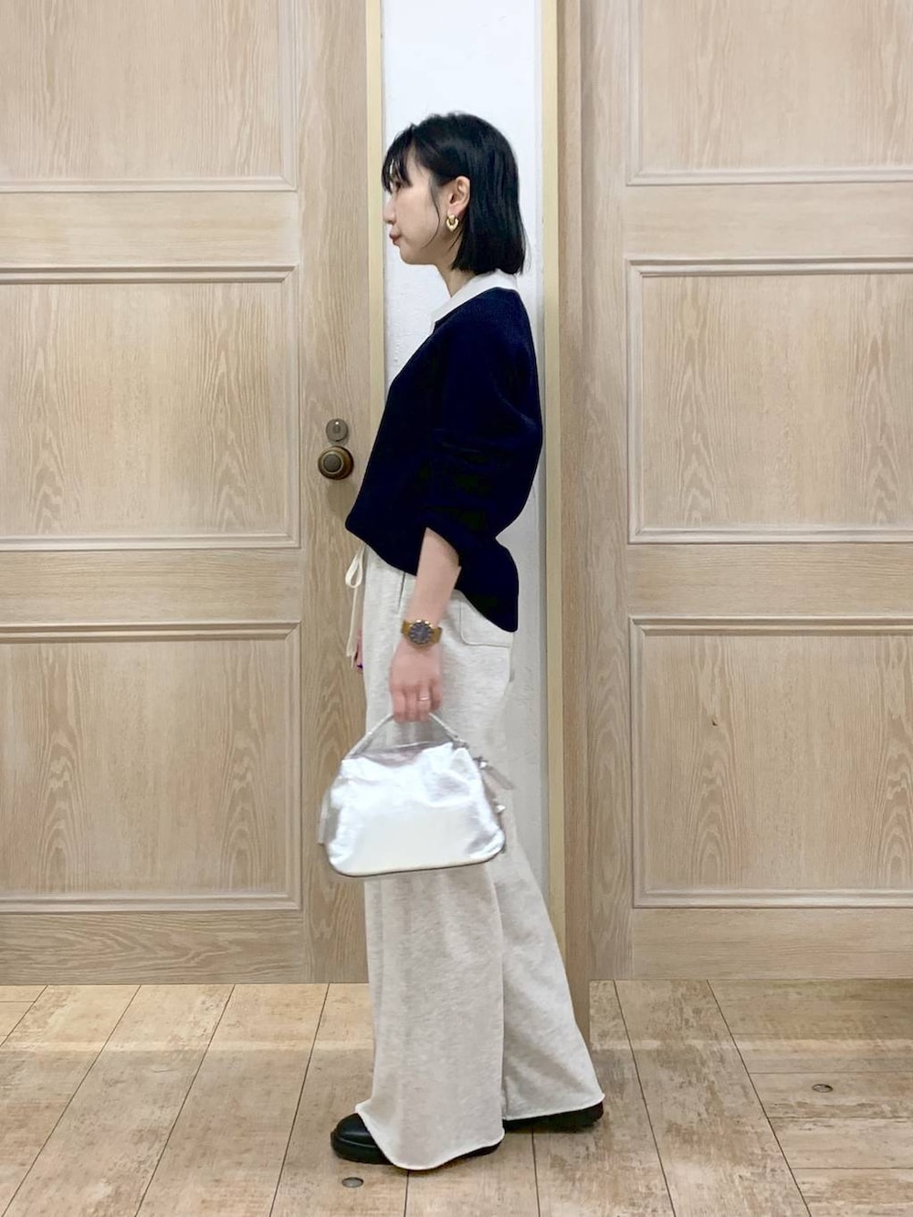 シルバー系のショルダーバッグ、ブラック系のブーツ、ホワイト系のスウェットパンツを着用したレディースの冬コーディネートの2枚目の写真