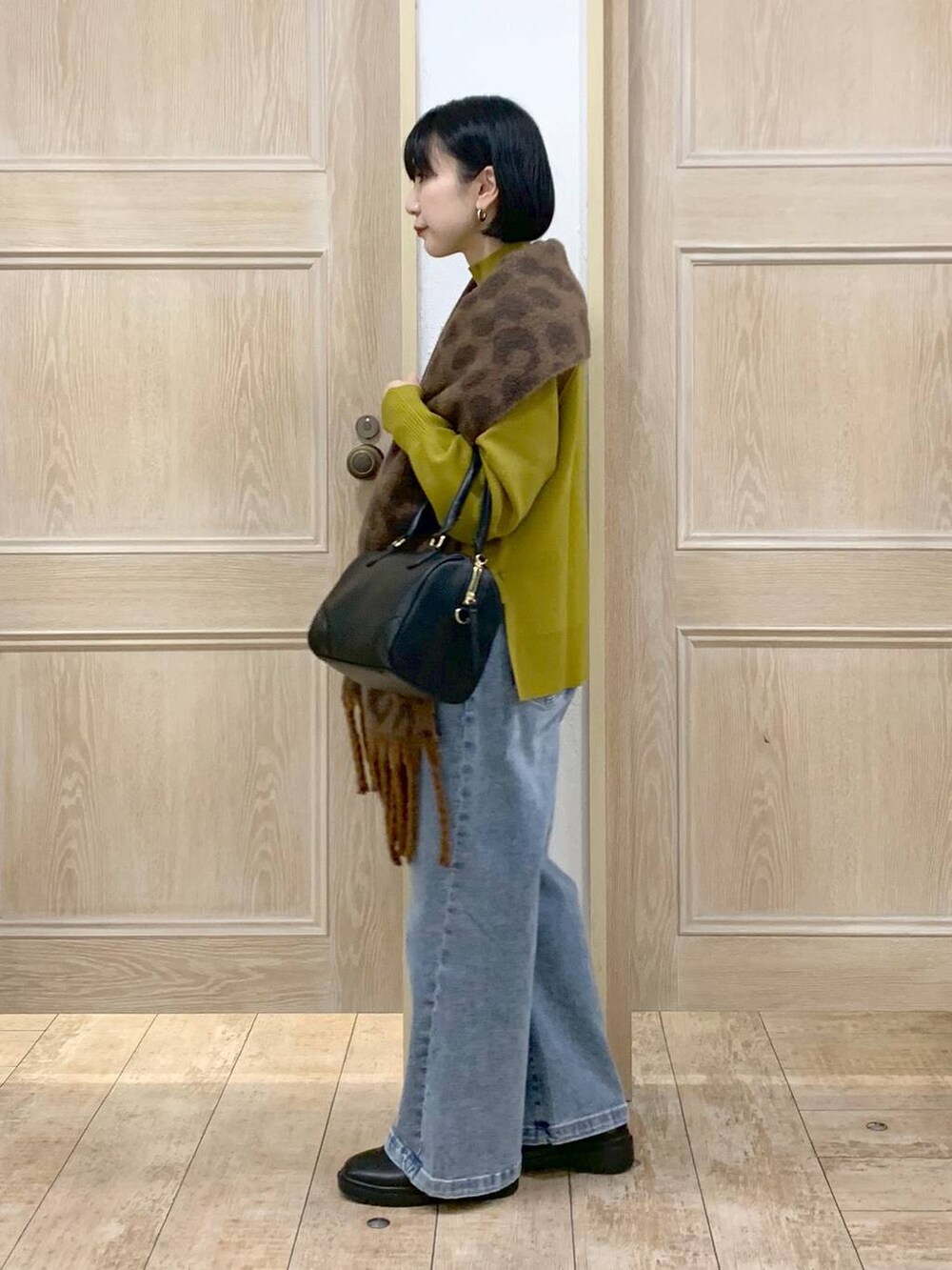 イエロー系のニット/セーター、ブラック系のボストンバッグ、ブルー系のデニムパンツを着用したレディースの秋コーディネートの2枚目の写真