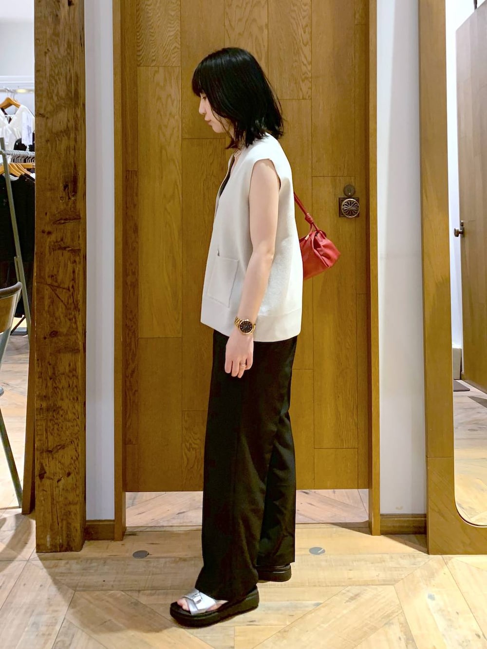 レッド系のショルダーバッグ、ホワイト系のベスト、ブラック系のその他パンツを着用したレディースの夏コーディネートの2枚目の写真