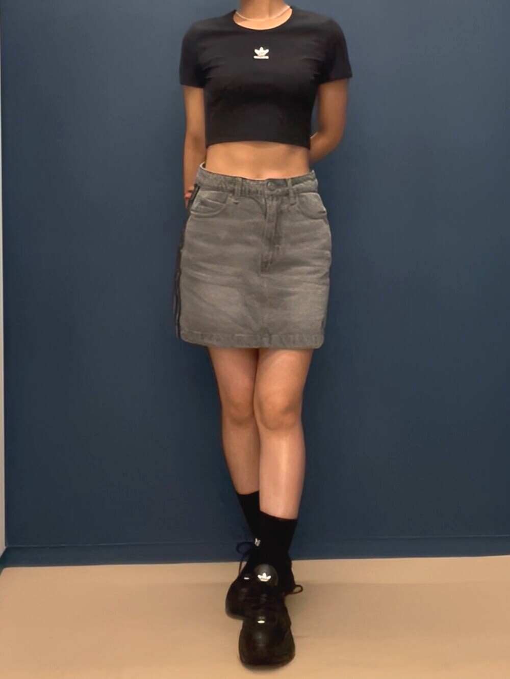 ブラック系のスニーカー、グレー系のデニムスカート、ブラック系のTシャツ/カットソーを着用したレディースの夏コーディネートの2枚目の写真