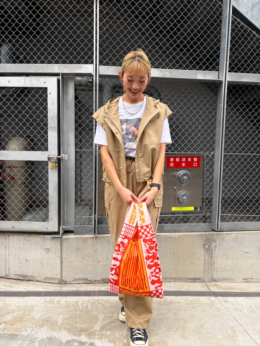 ベージュ系のベスト、ベージュ系のカーゴパンツ、オレンジ系のエコバッグ/サブバッグを着用したレディースの春コーディネートの2枚目の写真