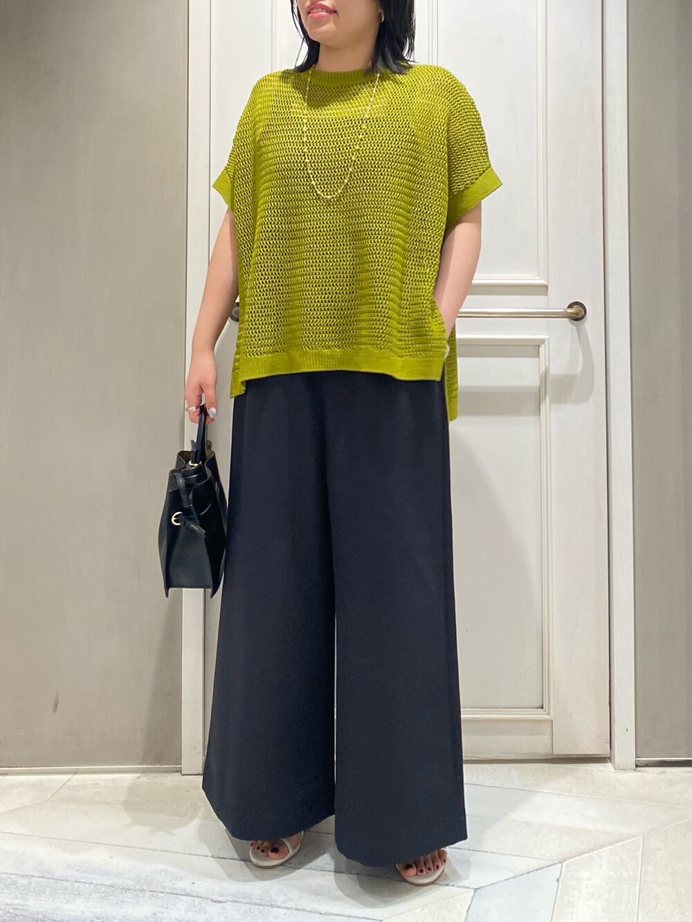 イエロー系のニット/セーター、ブラック系のつなぎ/オールインワン、ホワイト系のサンダルを着用したレディースの夏コーディネートの4枚目の写真