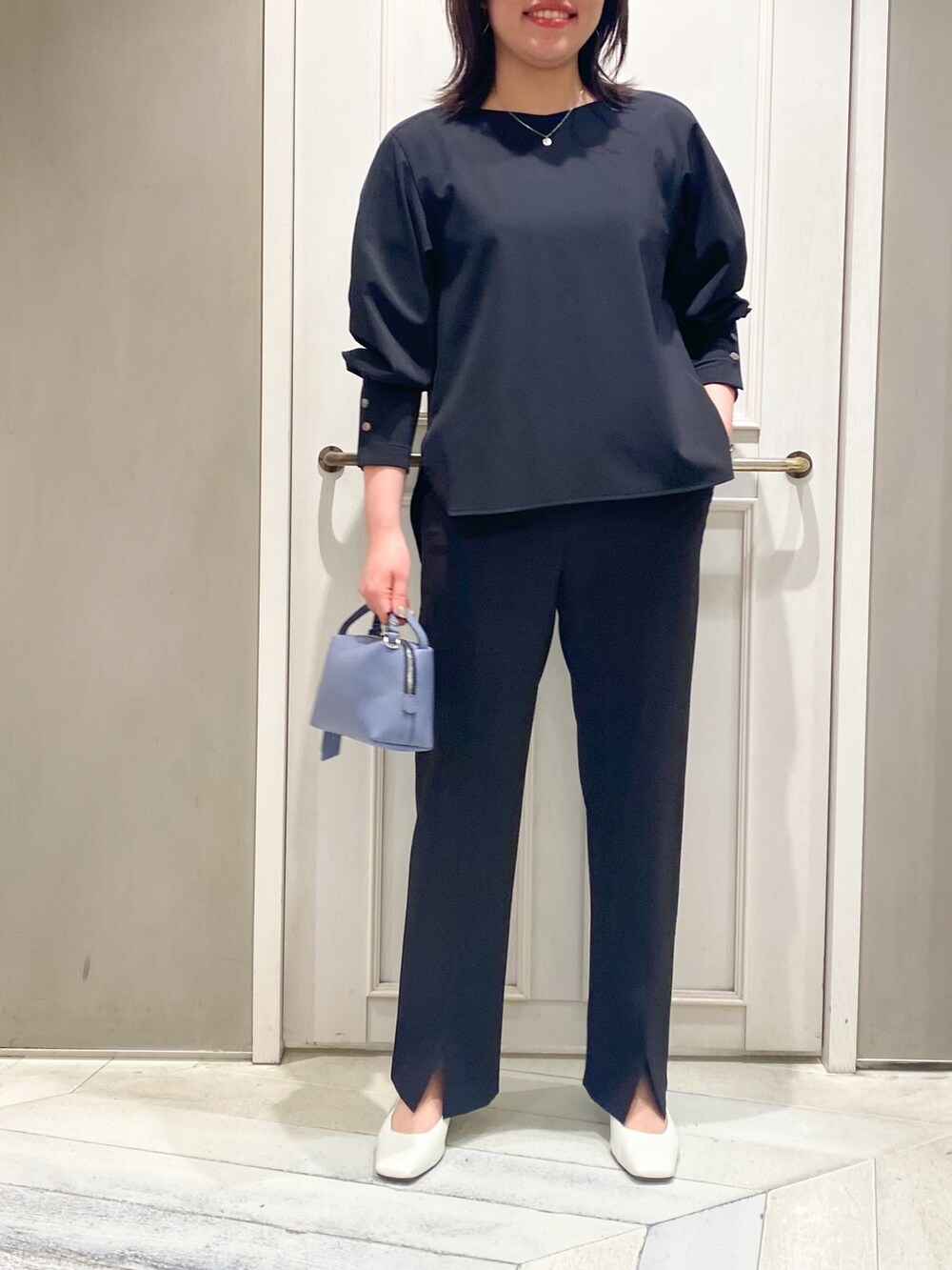 ブラック系のシャツ/ブラウス、ブラック系のスラックス、ブルー系のハンドバッグを着用したレディースの春コーディネートの2枚目の写真