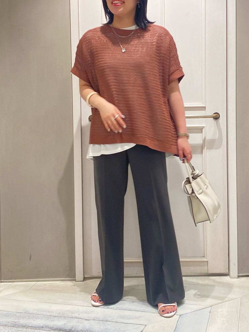 ブラウン系のニット/セーター、ホワイト系のTシャツ/カットソー、グレー系のスラックスを着用したレディースの夏コーディネートの3枚目の写真