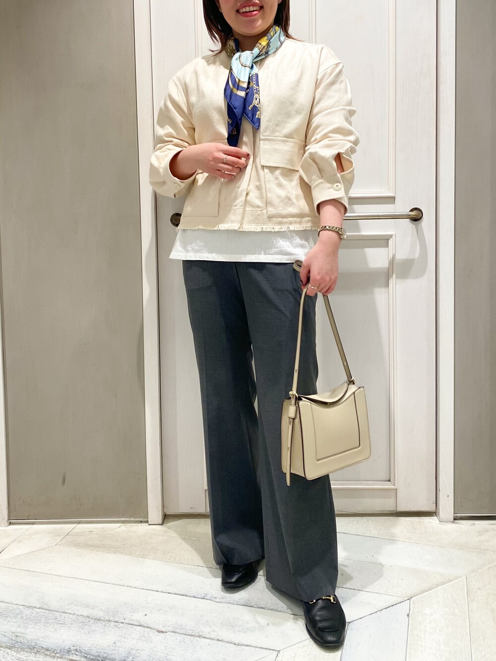 ホワイト系のブルゾン、ホワイト系のショルダーバッグ、グレー系のスラックスを着用したレディースの冬コーディネートの2枚目の写真