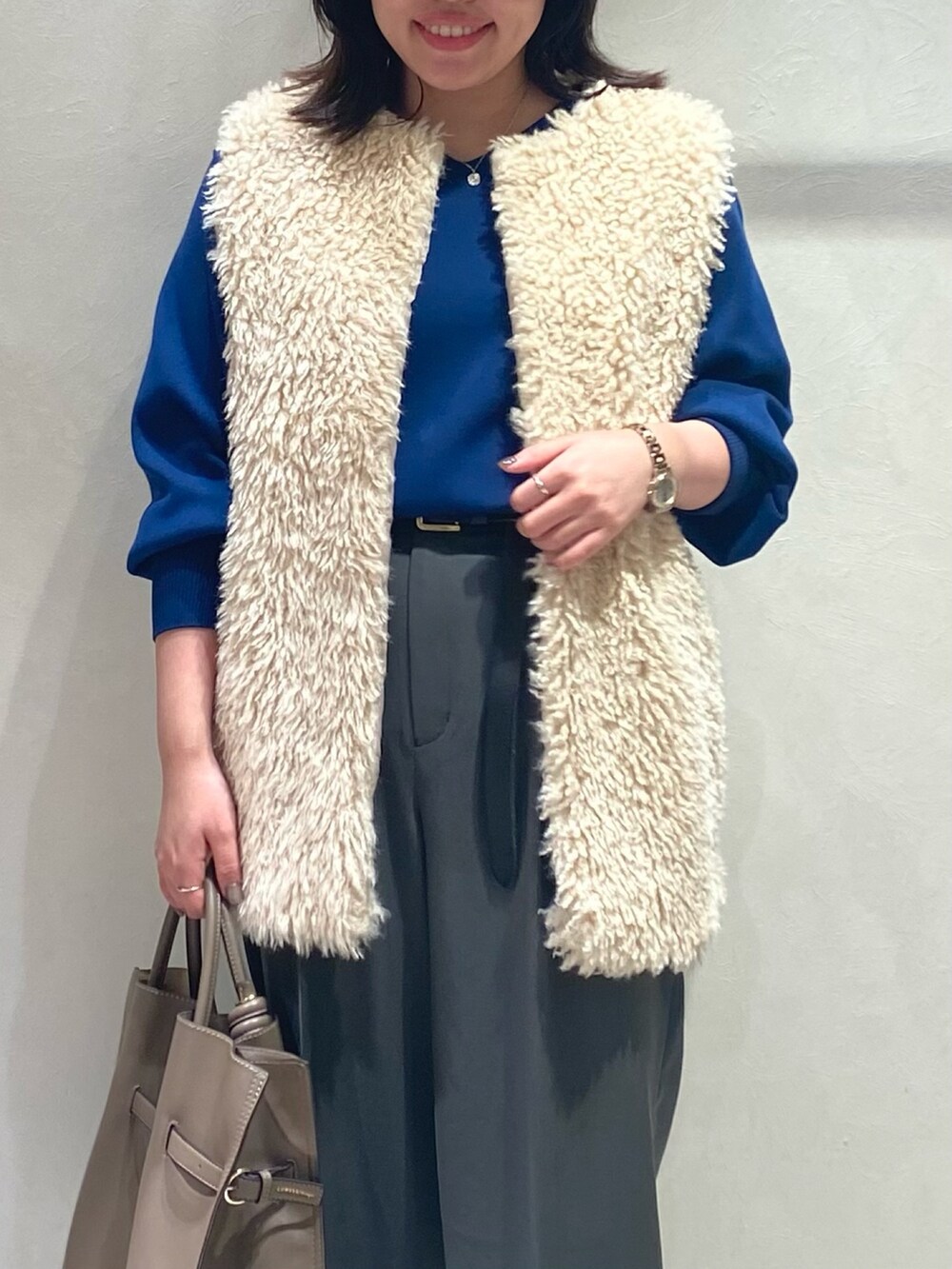 グレー系のスラックス、ホワイト系のベスト、ブルー系のニット/セーターを着用したレディースの秋コーディネートの5枚目の写真