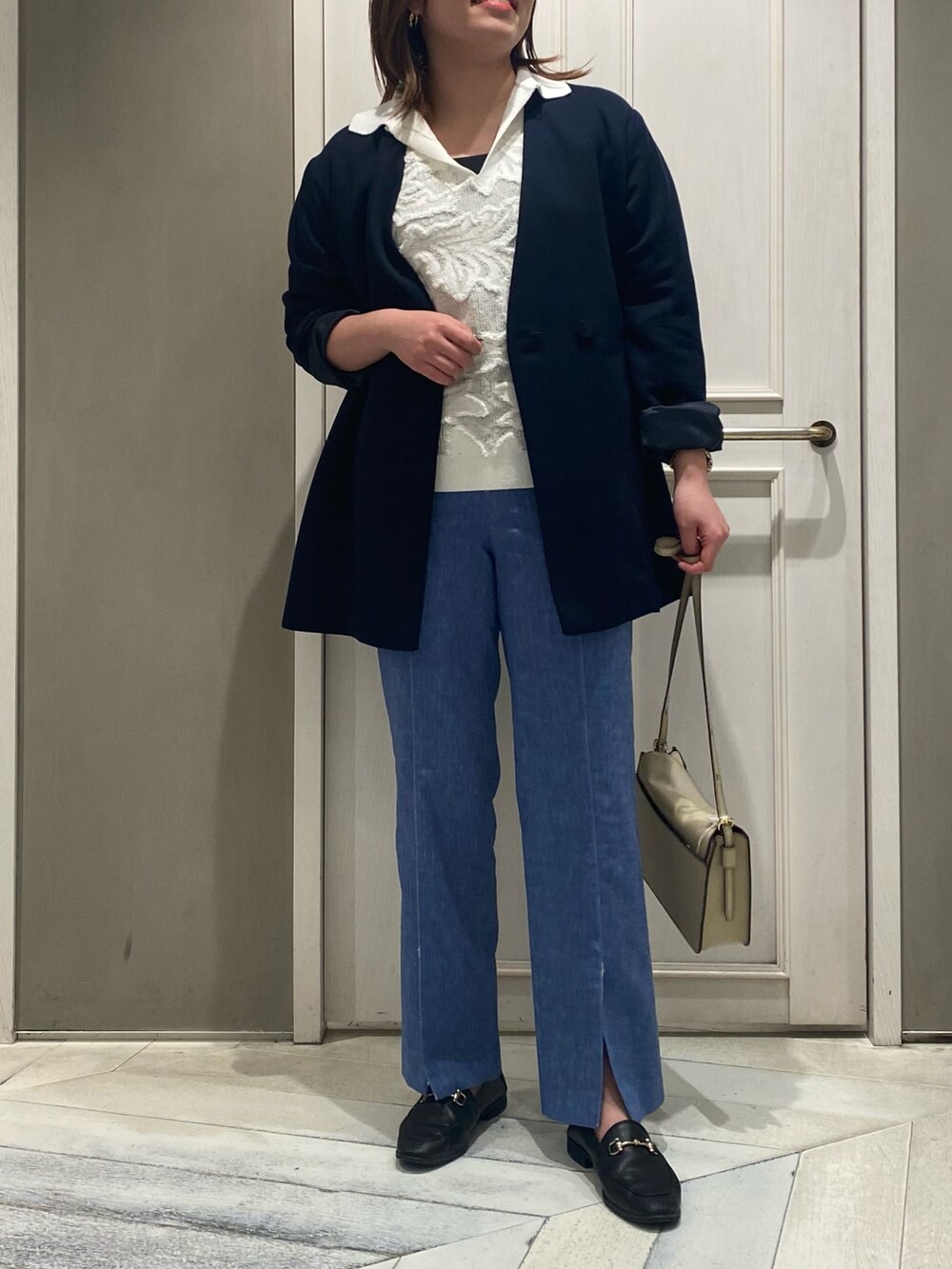 ベージュ系のノーカラーコート、ホワイト系のニット/セーター、ブルー系のデニムパンツを着用したレディースの春コーディネートの2枚目の写真