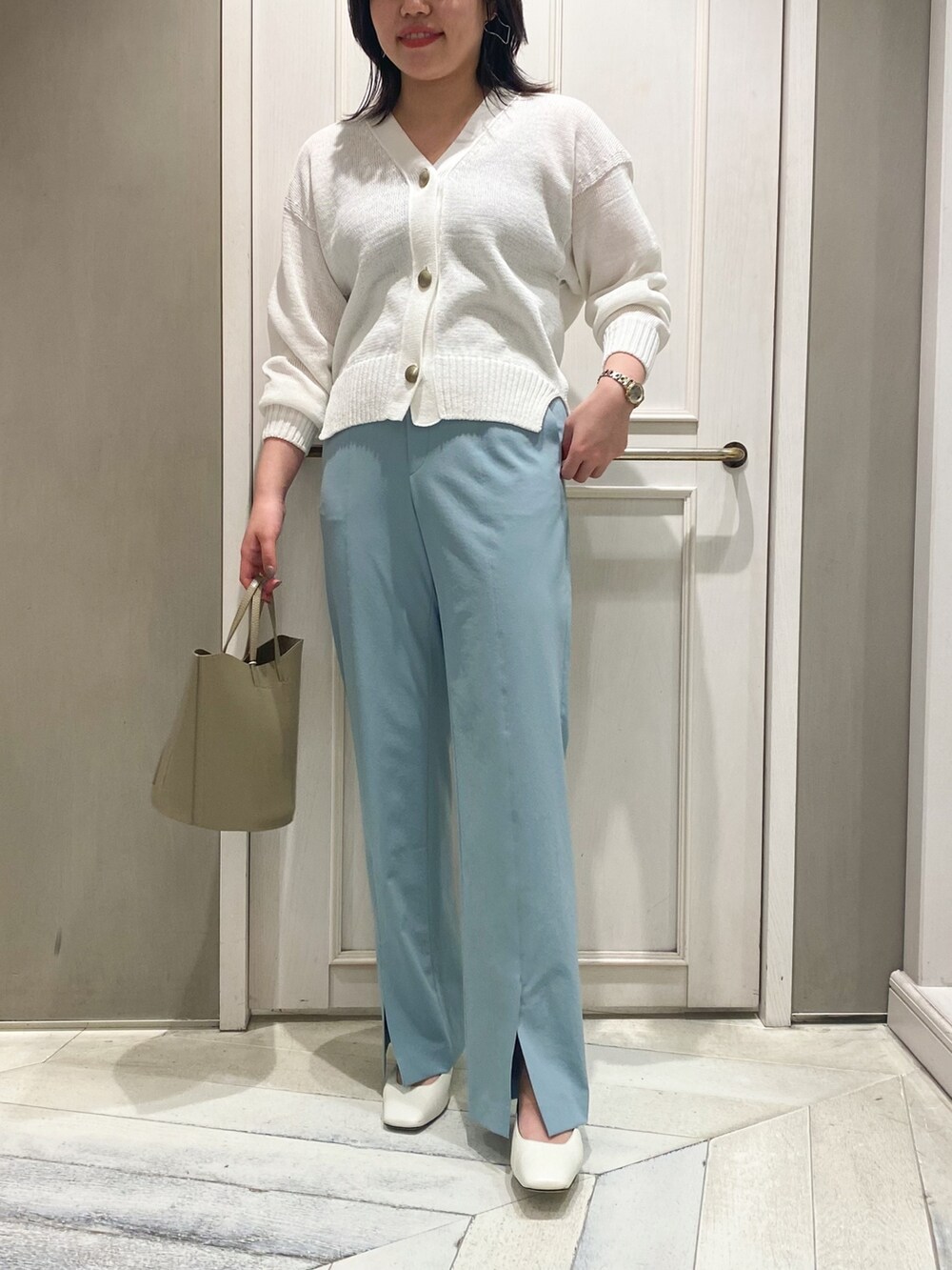 ホワイト系のカーディガン/ボレロ、ベージュ系のハンドバッグ、ブルー系のスラックスを着用したレディースの春コーディネートの2枚目の写真