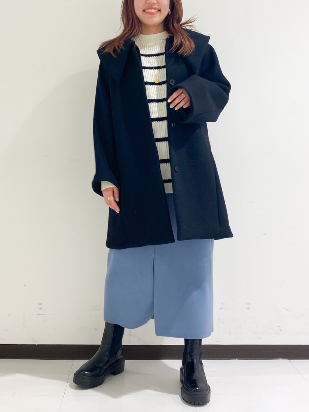 ブラック系のチェスターコート、ブラック系のブーツ、ブルー系のスカートを着用したレディースの冬コーディネートの2枚目の写真