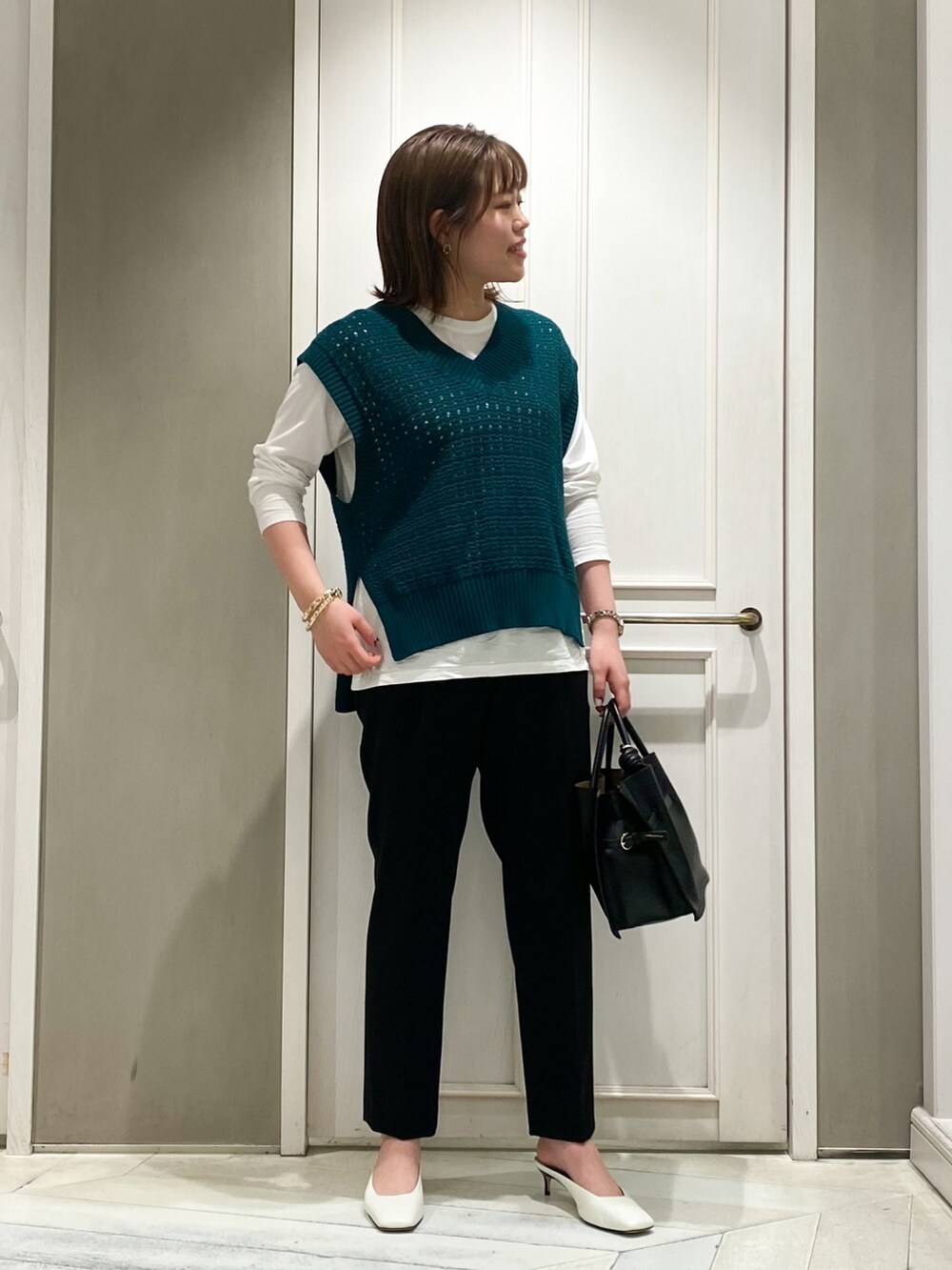 グリーン系のニット/セーター、ブラック系のサロペット/オーバーオール、ホワイト系のハンドバッグを着用したレディースの春コーディネートの3枚目の写真