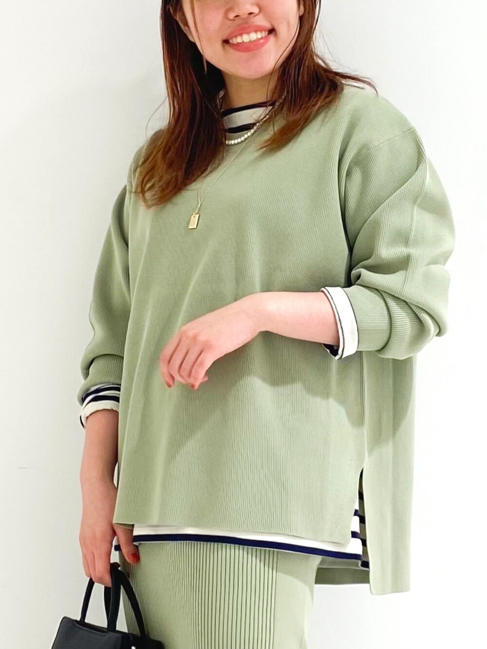 グリーン系のニット/セーター、グリーン系のスカート、ブラウン系のハンドバッグを着用したレディースの秋コーディネートの2枚目の写真