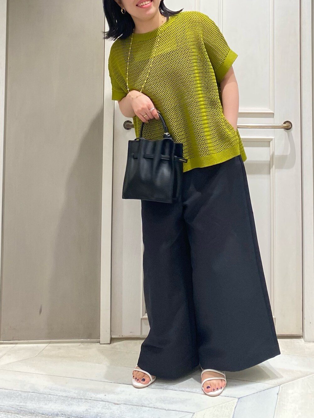 イエロー系のニット/セーター、ブラック系のつなぎ/オールインワン、ホワイト系のサンダルを着用したレディースの夏コーディネートの3枚目の写真