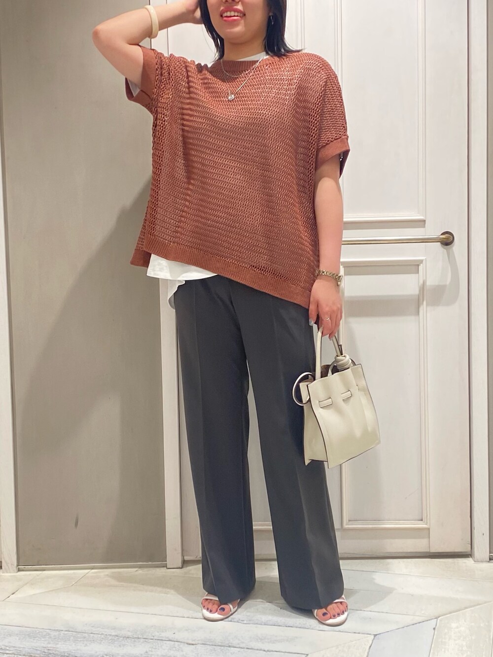ブラウン系のニット/セーター、ホワイト系のTシャツ/カットソー、グレー系のスラックスを着用したレディースの夏コーディネートの4枚目の写真