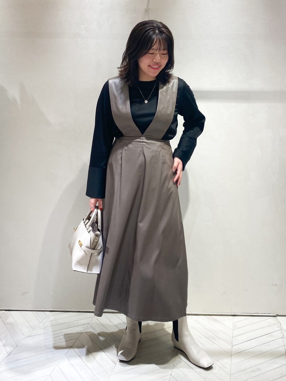 ブラウン系のジャンパースカート、ブラック系のTシャツ/カットソー、ホワイト系のショルダーバッグを着用したレディースの秋コーディネートの2枚目の写真