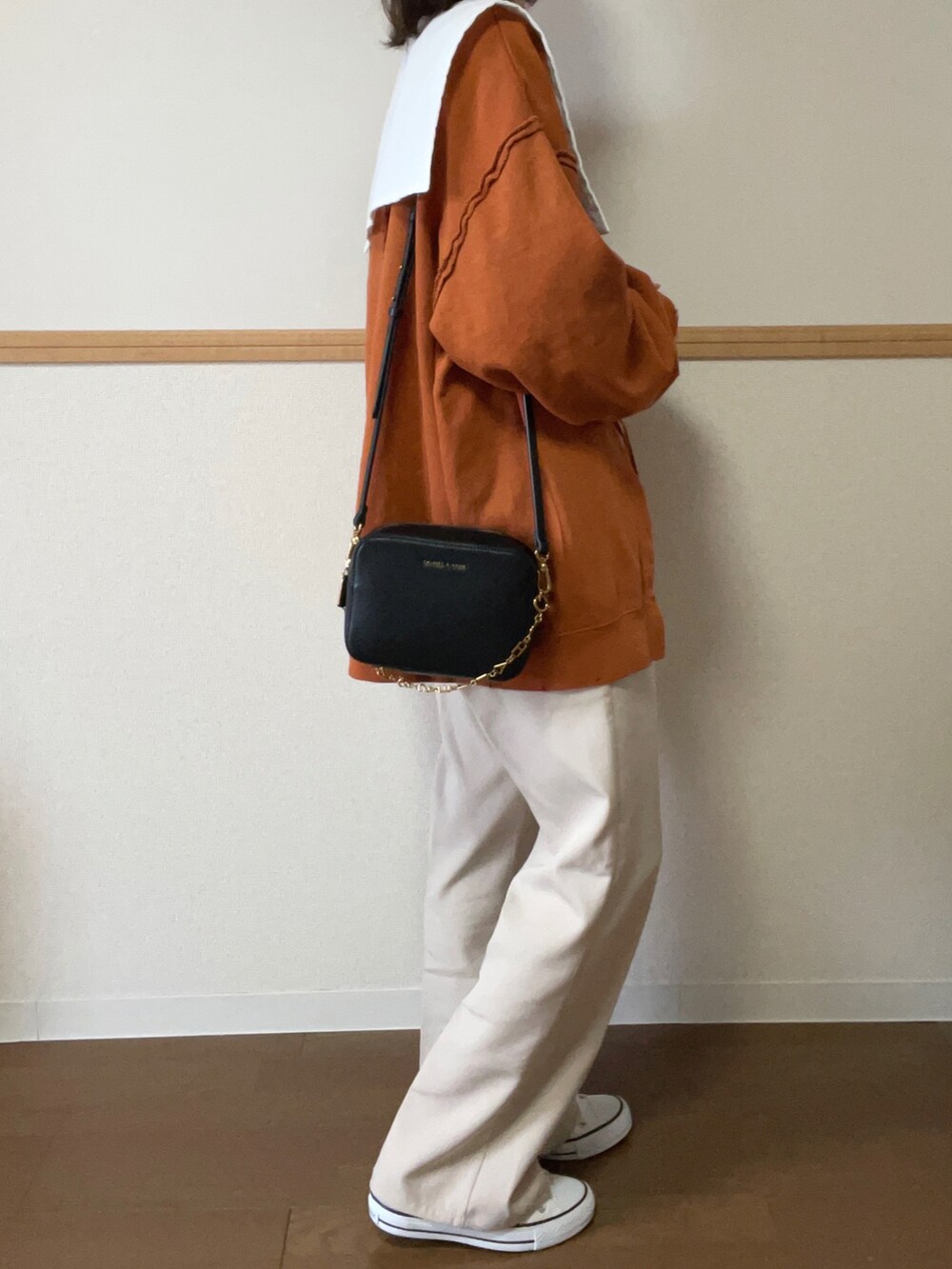 オレンジ系のスウェット、ホワイト系のシャツ/ブラウス、ホワイト系のスラックスを着用したレディースの秋コーディネートの2枚目の写真