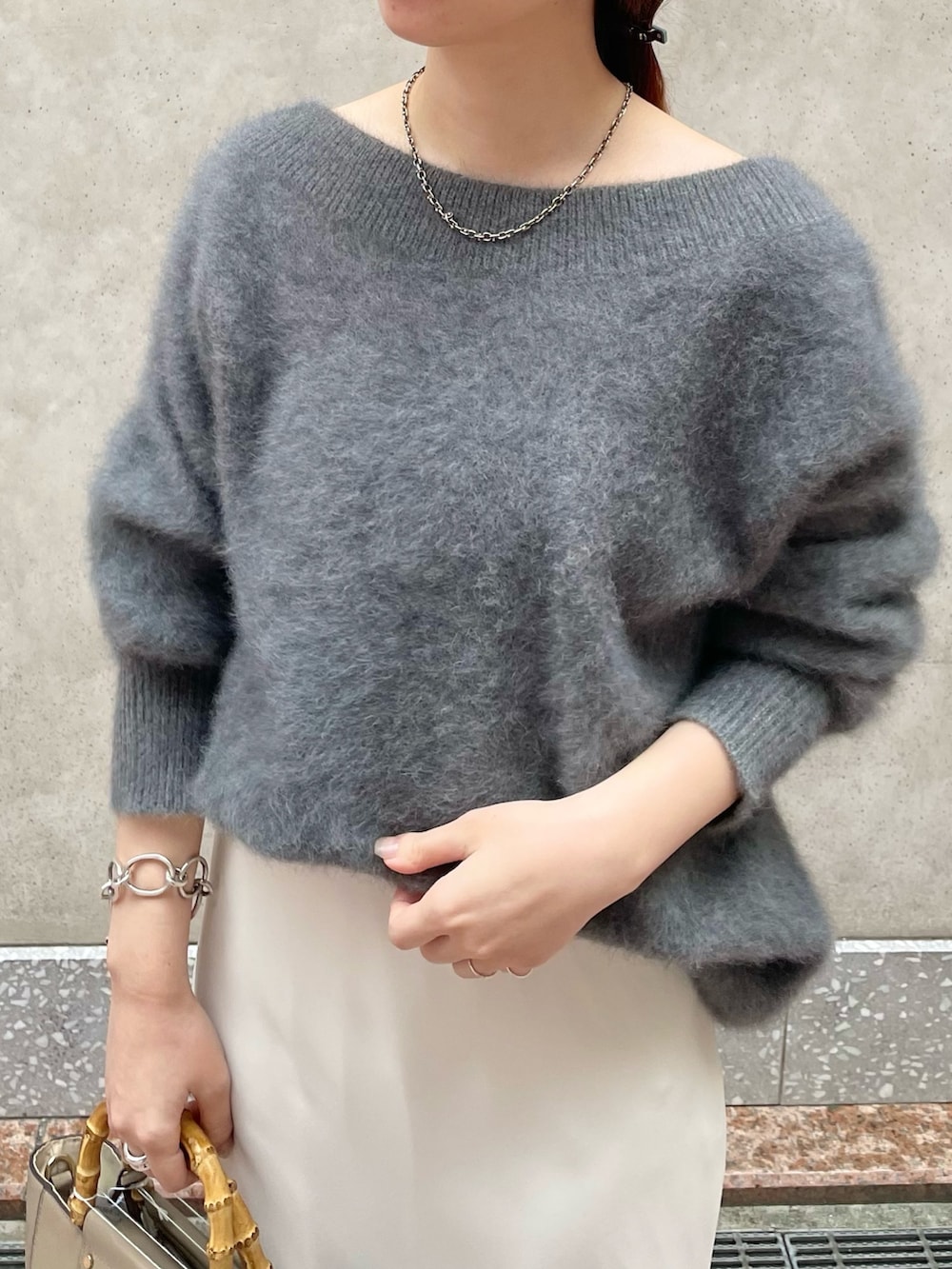 グレー系のニット/セーター、ホワイト系のスカート、ベージュ系のショルダーバッグを着用したレディースの秋コーディネートの2枚目の写真