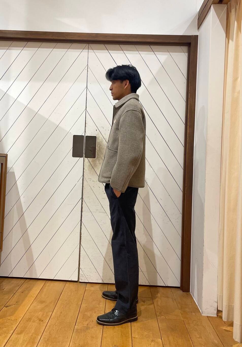 オレンジ系のニット/セーター、グレー系のその他パンツ、ベージュ系のカバーオールを着用したメンズの冬コーディネートの2枚目の写真