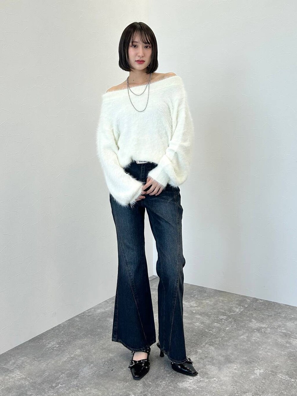 ブルー系のデニムパンツ、ブラック系のパンプス、ホワイト系のニット/セーターを着用したレディースの秋コーディネートの2枚目の写真