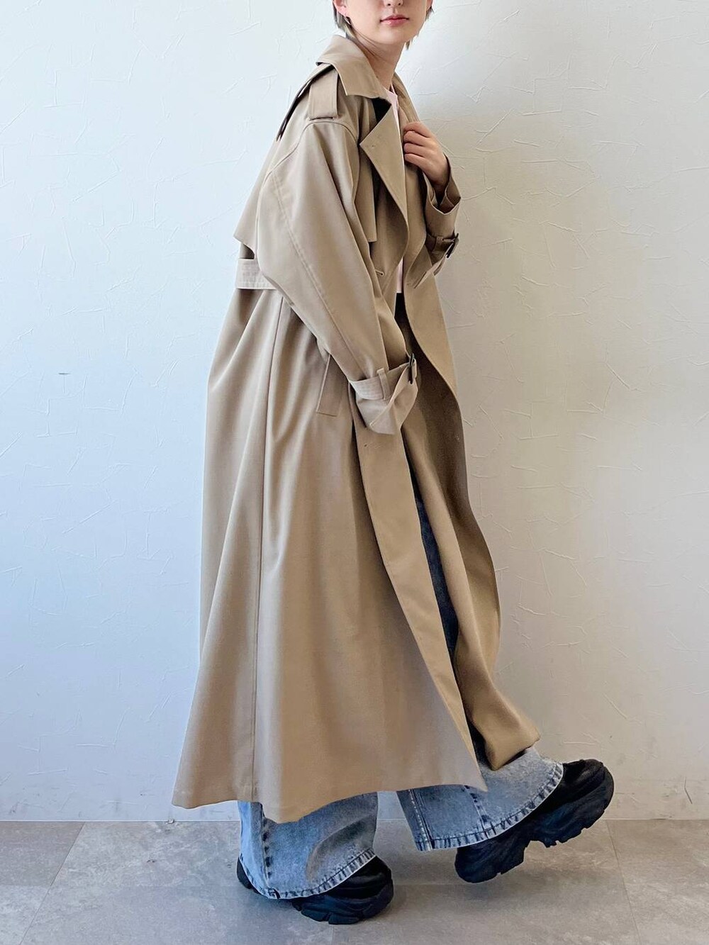 ブラック系のスニーカー、ベージュ系のトレンチコート、ブルー系のデニムパンツを着用したレディースの春コーディネートの3枚目の写真