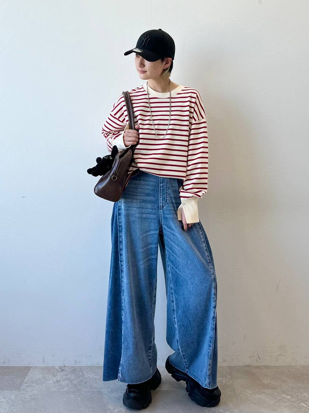 ブラック系のスニーカー、ブラウン系のボストンバッグ、ブルー系のデニムパンツを着用したレディースの春コーディネートの2枚目の写真