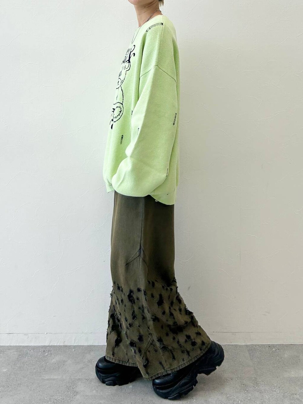 ブラック系のデニムパンツ、ブラック系のブーツ、グリーン系のニット/セーターを着用したレディースの秋コーディネートの4枚目の写真