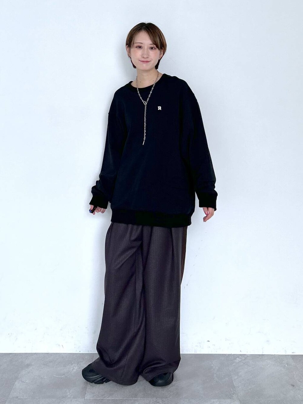 ブラウン系のスラックス、ブラック系のスウェット、シルバー系のピアス（両耳用）を着用したレディースの夏コーディネートの7枚目の写真