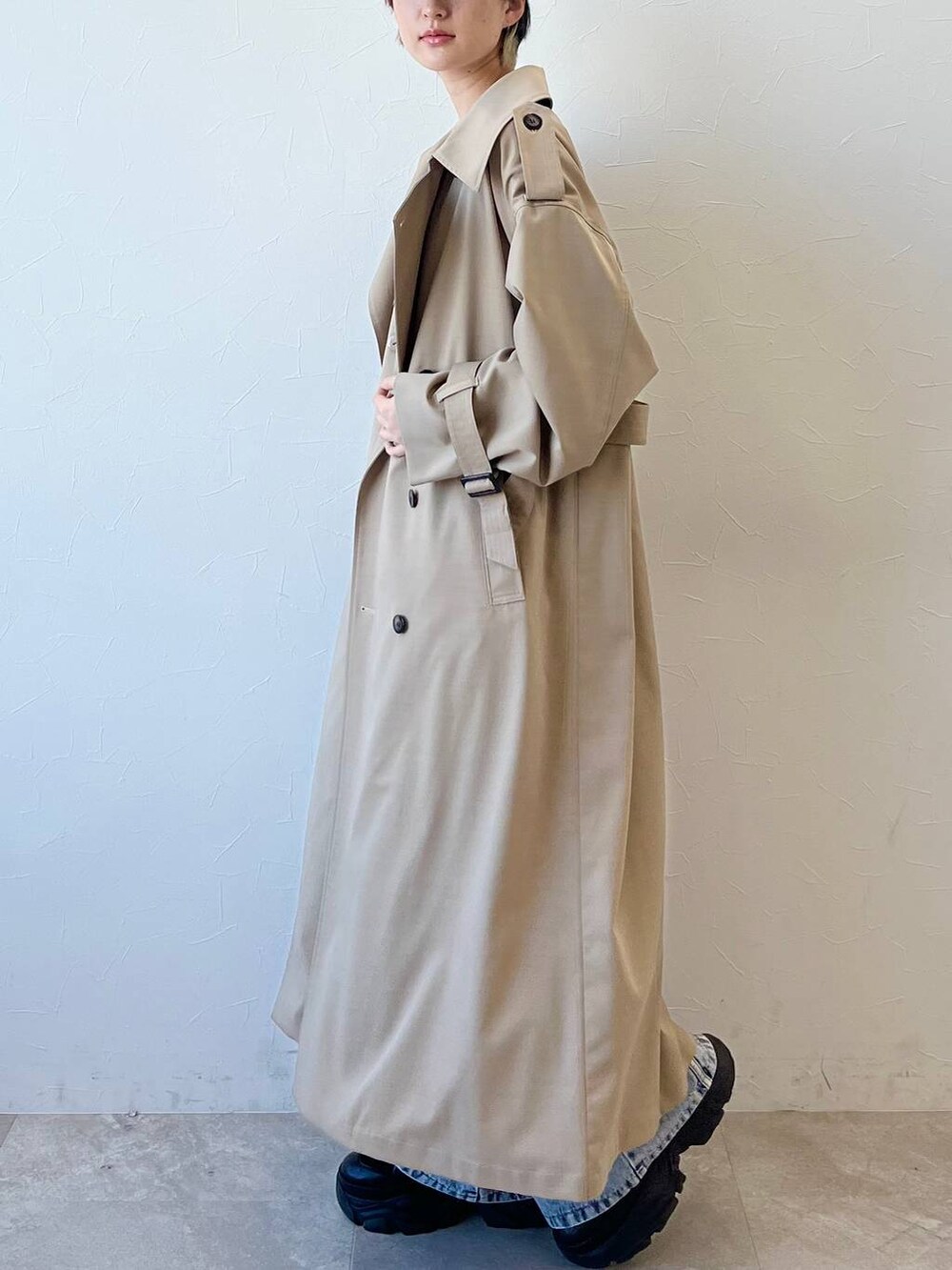 ブラック系のスニーカー、ベージュ系のトレンチコート、ブルー系のデニムパンツを着用したレディースの春コーディネートの5枚目の写真