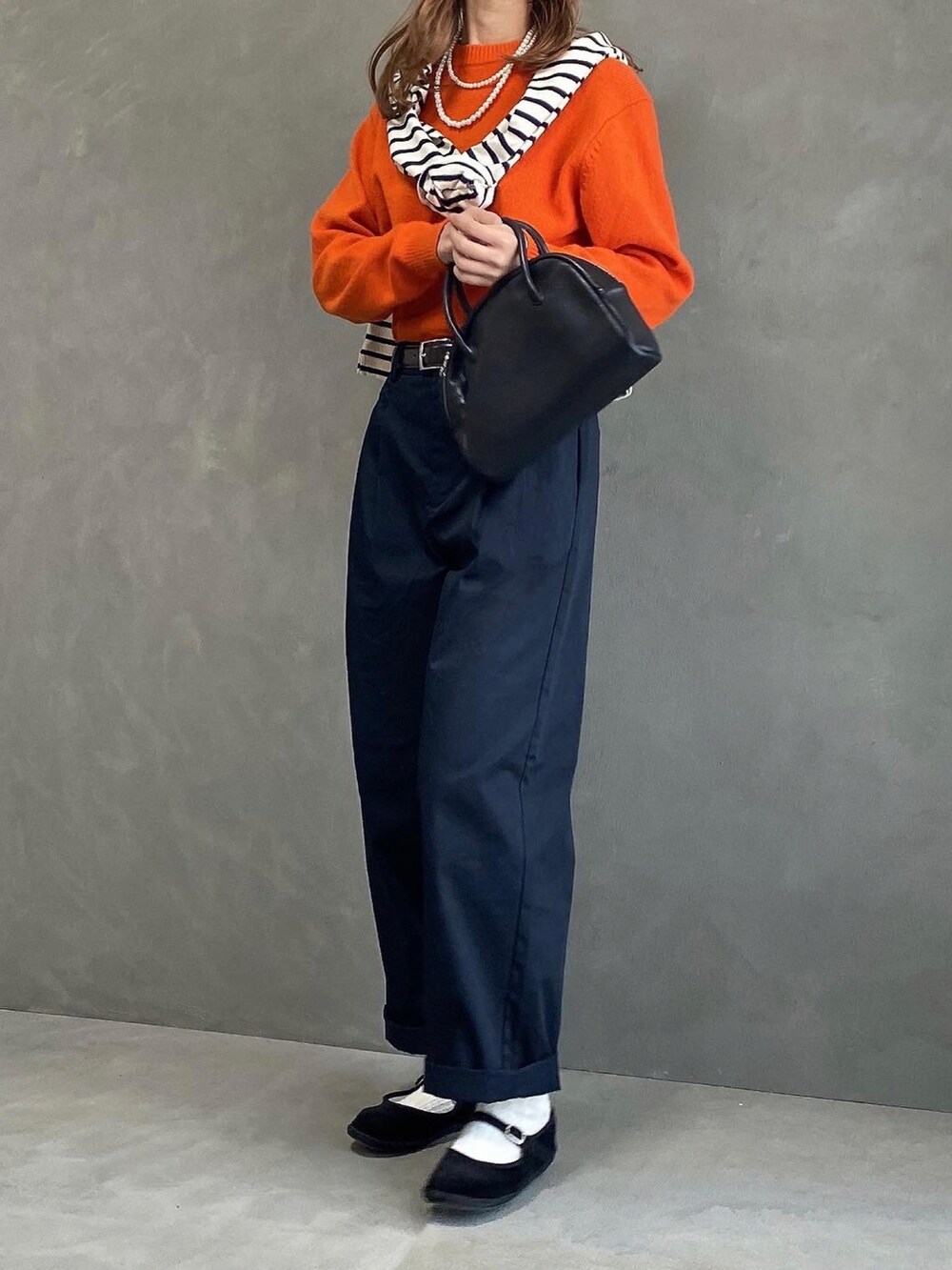 ブラック系のチノパンツ、オレンジ系のニット/セーター、ブラック系のボストンバッグを着用したレディースの春コーディネートの2枚目の写真